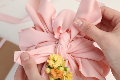 Photo of Furoshiki technique. Woman wrapping gift in pink fabric with flowers at white table, closeup