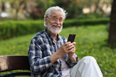 Portrait of happy grandpa with glasses using smartphone on bench in park