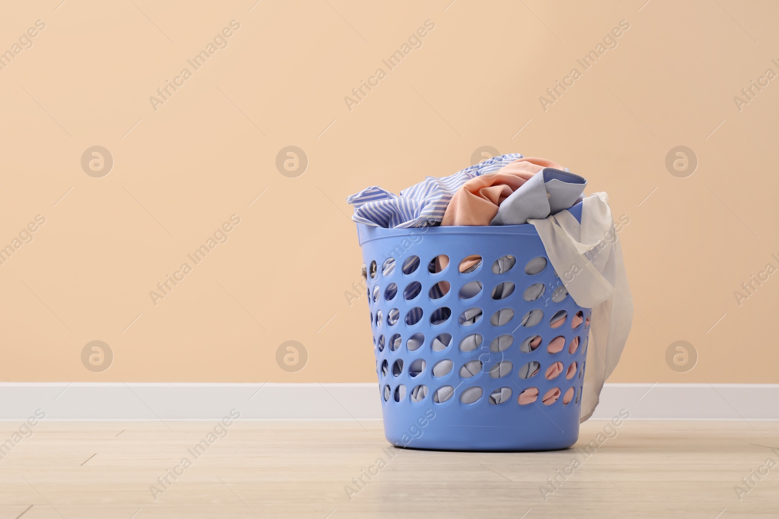 Photo of Laundry basket with clothes near beige wall indoors. Space for text