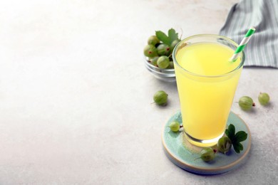 Photo of Tasty gooseberry juice in glass and fresh berries on light table. Space for text