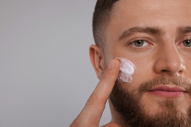 Photo of Handsome man applying cream onto his face on light grey background, closeup. Space for text