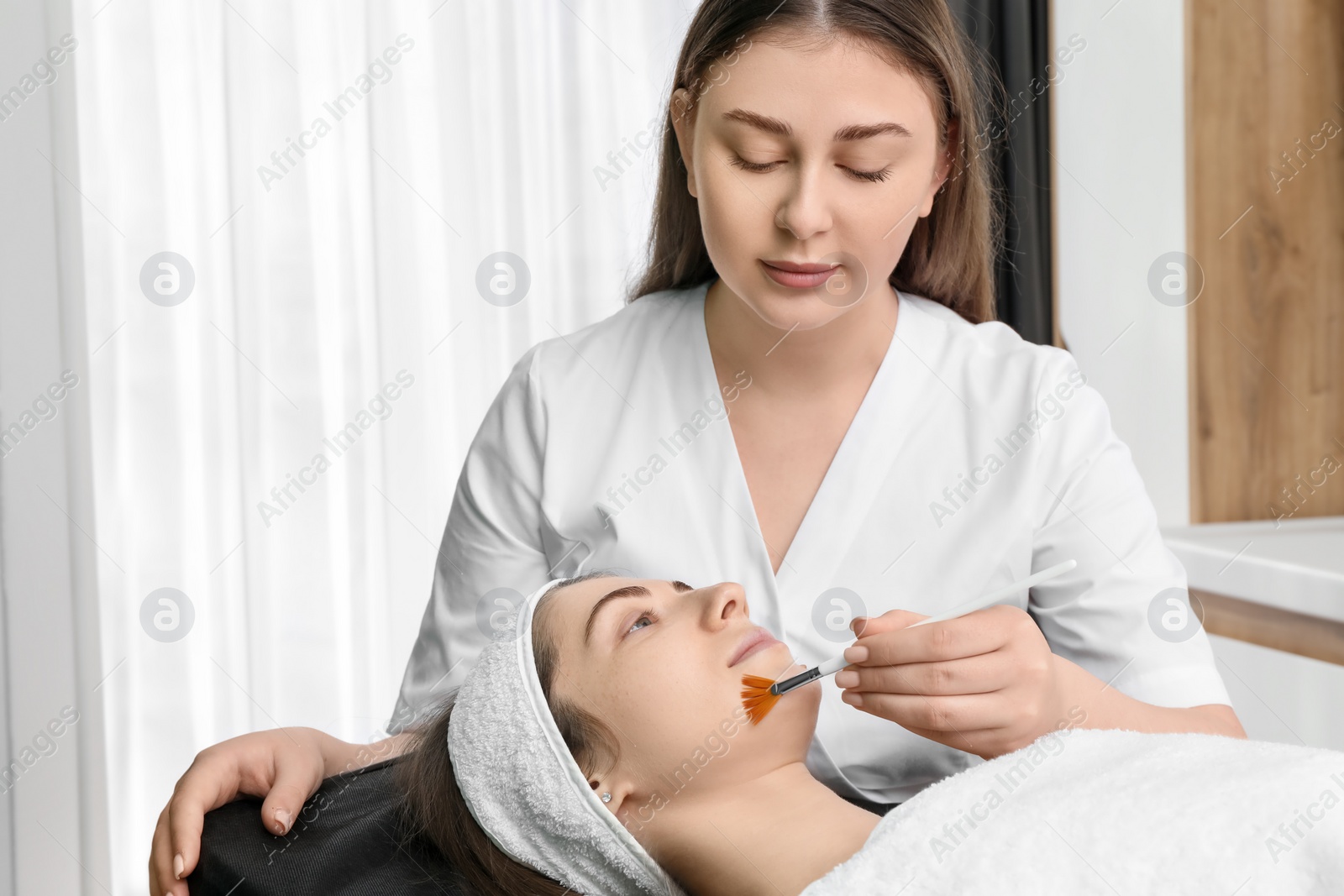 Photo of Cosmetologist with brush applying cosmetic product to client`s face in clinic