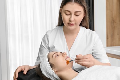 Photo of Cosmetologist with brush applying cosmetic product to client`s face in clinic