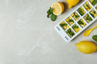 Photo of Ice cube tray with mint and lemon on grey background, top view. Space for text