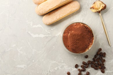 Photo of Tasty tiramisu in glass, coffee beans, spoon and biscuits on light grey table, flat lay. Space for text