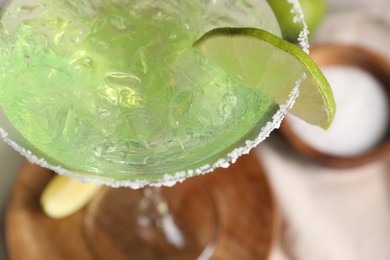 Delicious Margarita cocktail with ice cubes in glass and lime on table, closeup