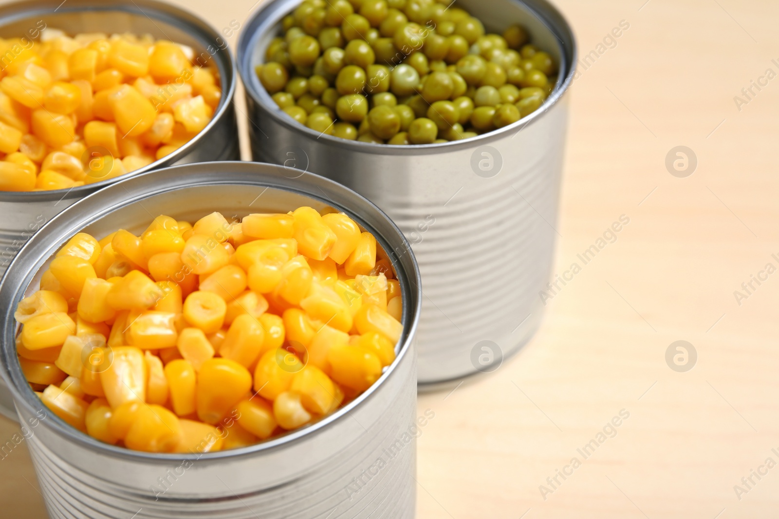 Photo of Open tin cans of sweet corn and peas on table, closeup. Space for text