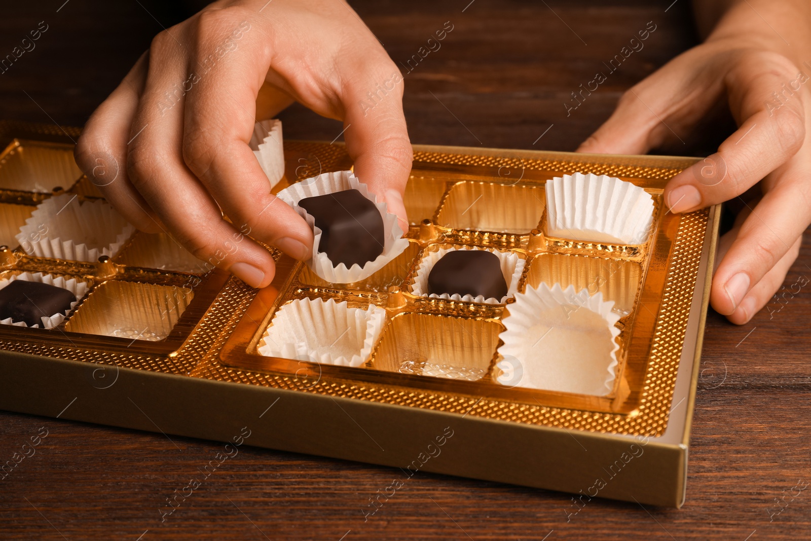 Photo of Woman taking chocolate candy out from box at wooden table, closeup