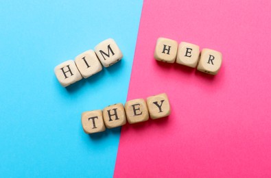 Photo of Gender pronouns made of wooden cubes on color background, flat lay