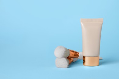 Tube of skin foundation and brushes on light blue background, space for text. Makeup product