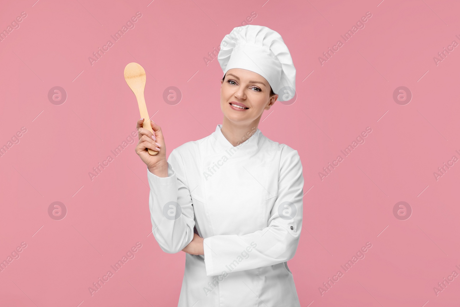 Photo of Happy chef in uniform holding wooden spoon on pink background