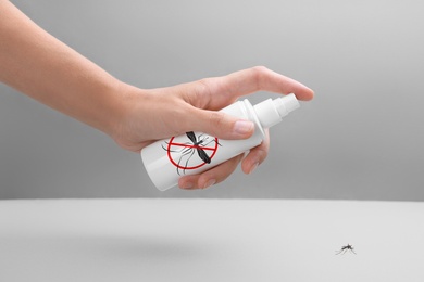 Woman spraying insect repellent on mosquito against grey background, closeup