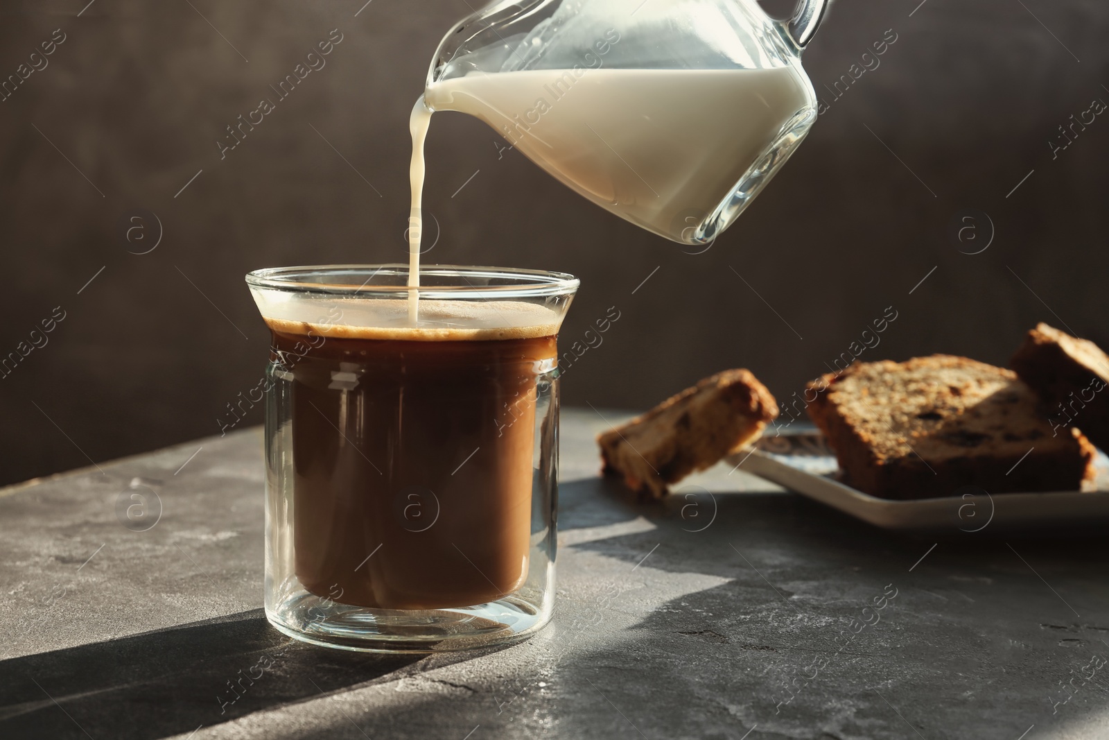 Photo of Adding milk to hot aromatic coffee on grey table. Space for text