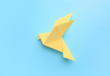 Photo of Origami art. Beautiful handmade paper bird on light blue background, top view