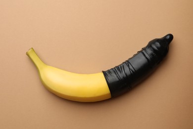 Photo of Banana with condom on pale orange background, top view. Safe sex concept