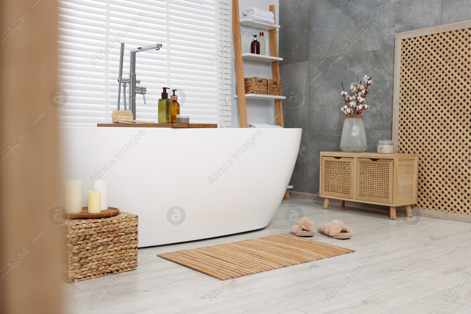 Photo of Stylish bathroom interior with bamboo bath mat and white tub