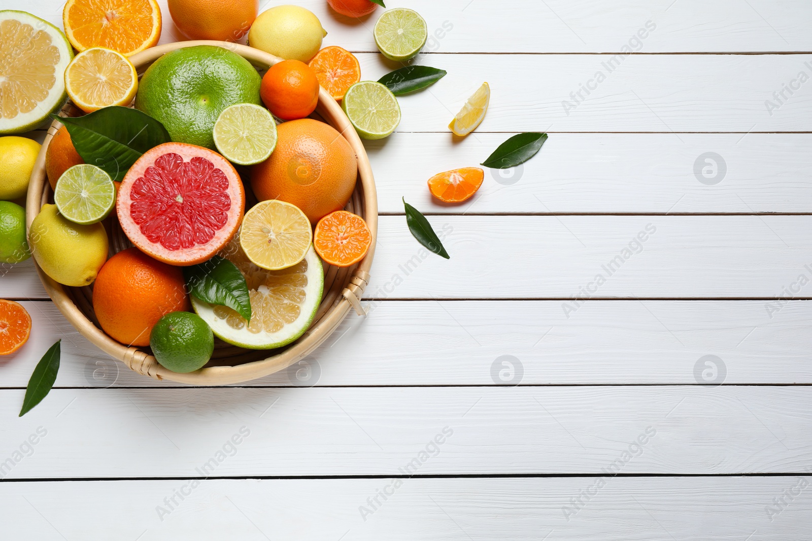 Photo of Different ripe citrus fruits with green leaves on white wooden table, flat lay. Space for text