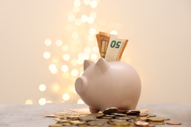 Piggy bank with euro banknote and coins on grey table against blurred lights