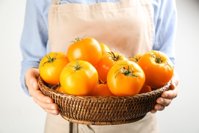 Photo of Woman holding wicker bowl of yellow tomatoes on light background, closeup