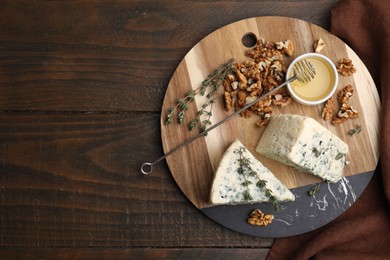 Photo of Tasty blue cheese with thyme, honey and walnuts on wooden table, top view. Space for text