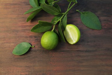 Branch with fresh leaves and limes on wooden table, closeup