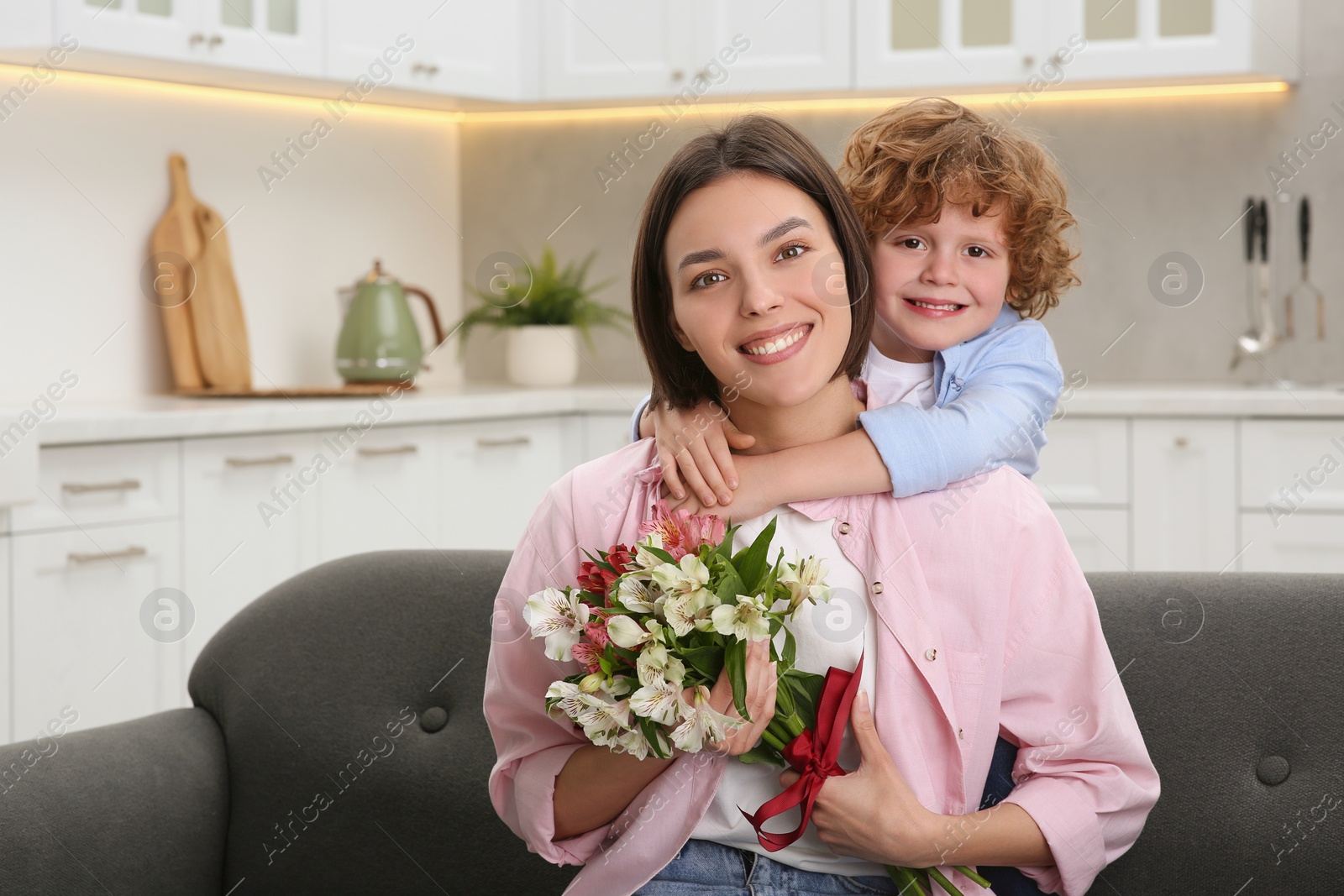 Photo of Little son congratulating his mom with Mother`s day at home, space for text. Woman holding bouquet of beautiful flowers