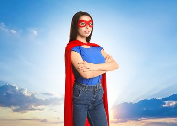 Image of Confident woman wearing superhero cape and mask against cloudy sky