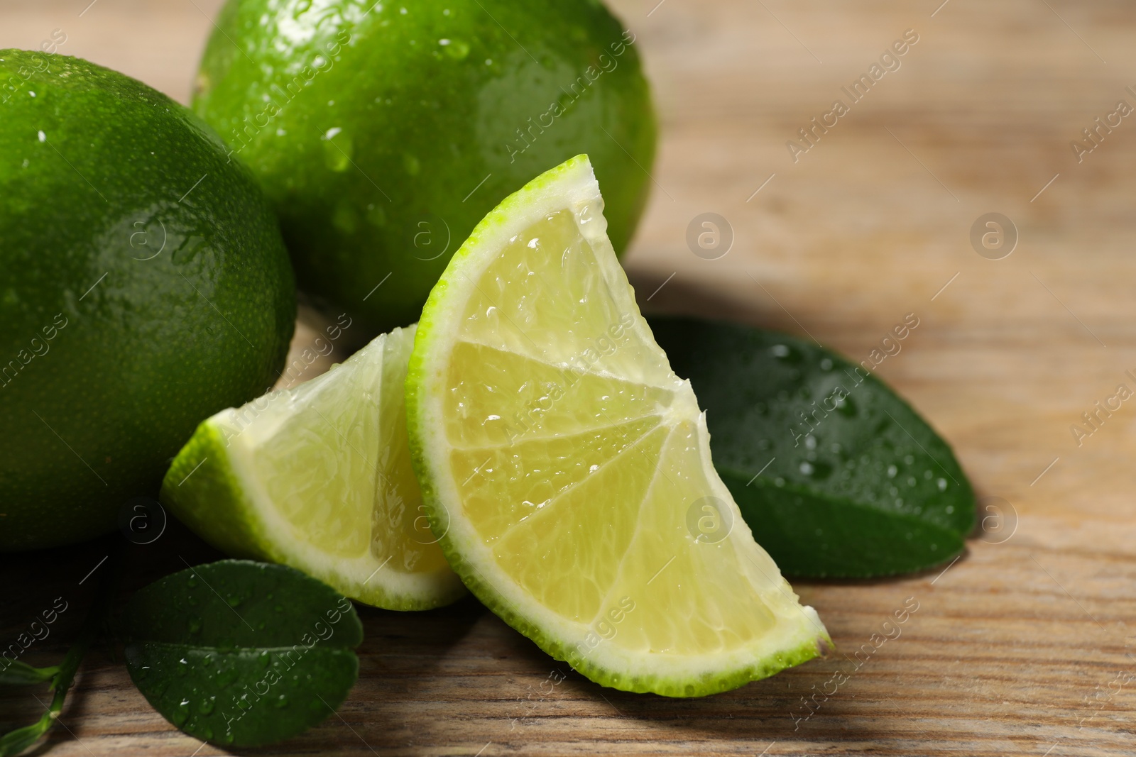 Photo of Fresh limes and green leaves with water drops on wooden table, closeup. Space for text