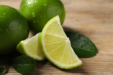 Fresh limes and green leaves with water drops on wooden table, closeup. Space for text