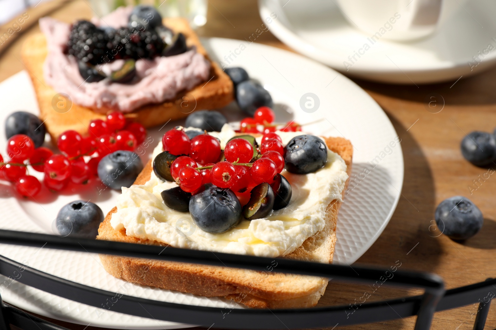 Photo of Sandwiches with cream cheese and berries on wooden tray