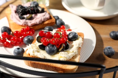 Photo of Sandwiches with cream cheese and berries on wooden tray