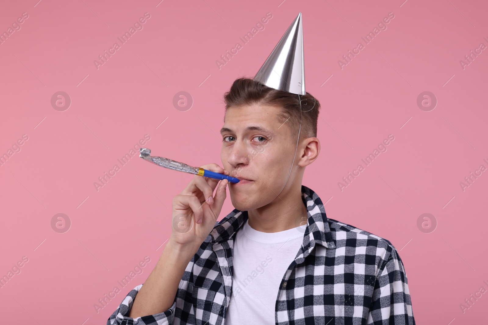 Photo of Young man in party hat with blower on pink background