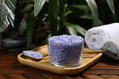 Photo of Bowl of purple sea salt, spoon and rolled towels on wooden table, closeup