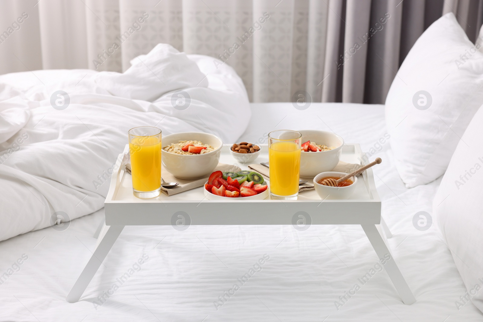 Tasty breakfast served in bed. Oatmeal, juice, fruits, almonds and honey on tray Photo of Tasty breakfast served in bed. Oatmeal, juice, fruits, almonds and honey on tray