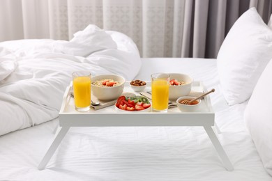Photo of Tasty breakfast served in bed. Oatmeal, juice, fruits, almonds and honey on tray