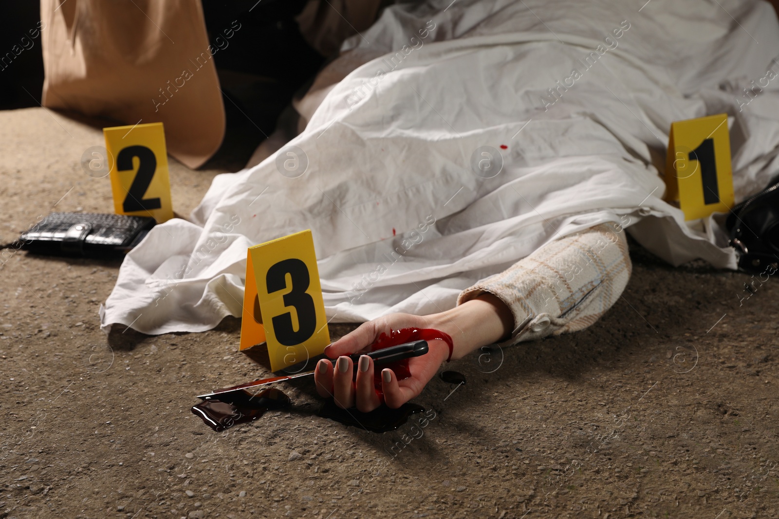 Photo of Crime scene with dead woman's body, bloody knife and markers outdoors, closeup