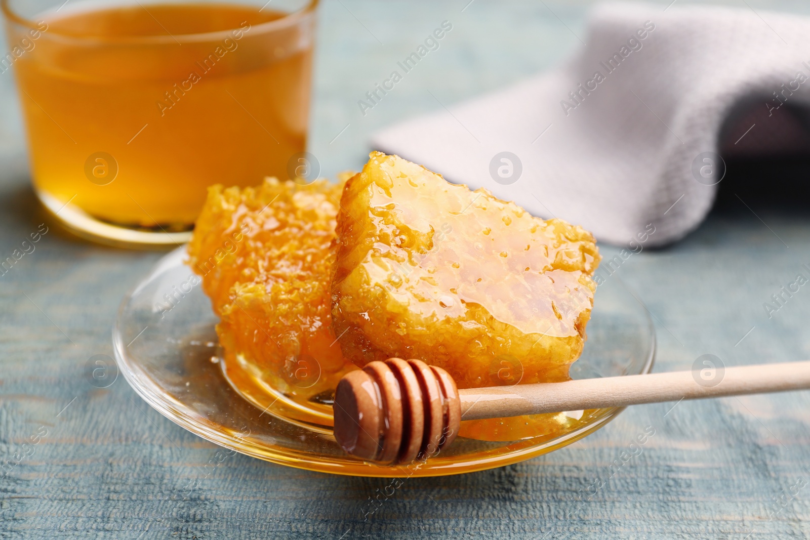 Photo of Tasty honey combs and dipper on light blue wooden table, closeup