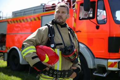 Firefighter in uniform with helmet near fire truck outdoors