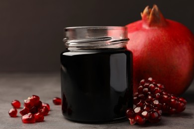 Photo of Glass jar of tasty pomegranate sauce and fresh ripe fruit on light grey table