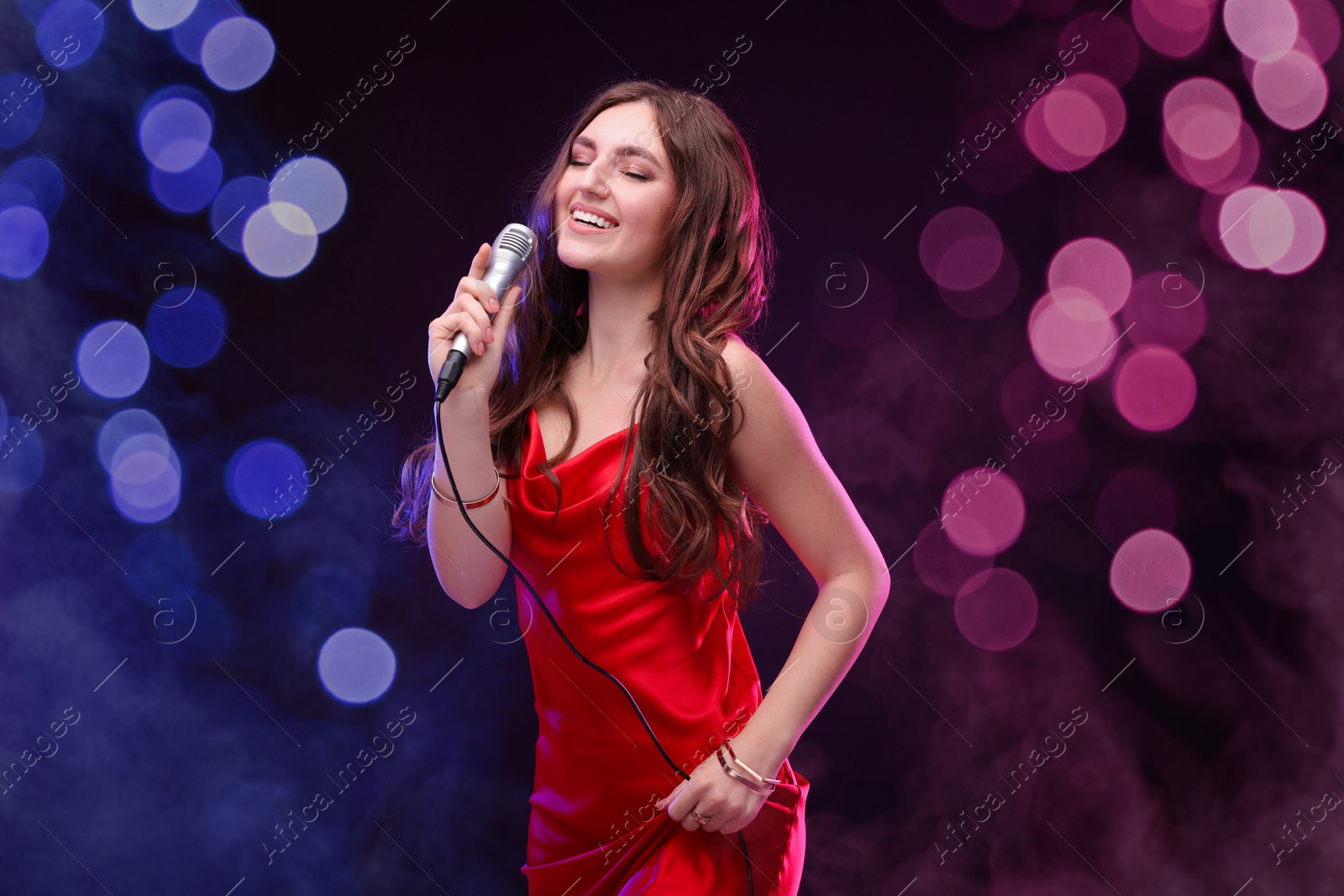 Image of Happy woman with microphone singing on stage in color lighted smoke