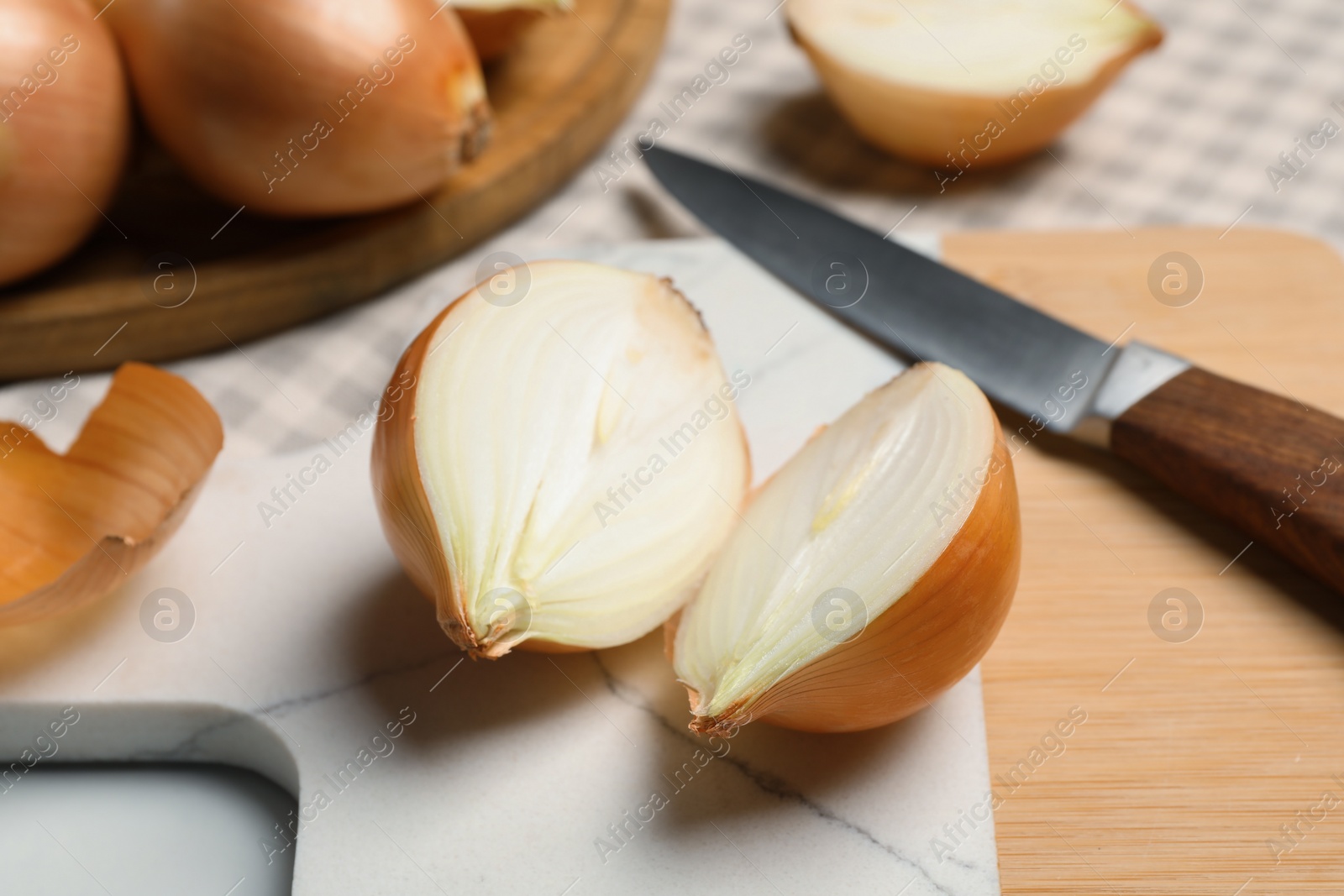 Photo of Whole and cut onions with knife on white table, closeup