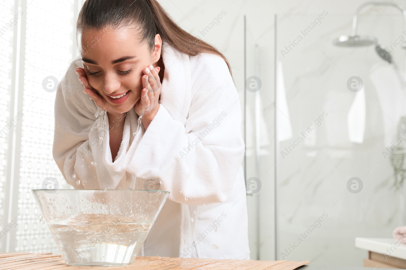 Photo of Beautiful young woman washing her face with water in bathroom, space for text