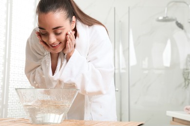 Photo of Beautiful young woman washing her face with water in bathroom, space for text