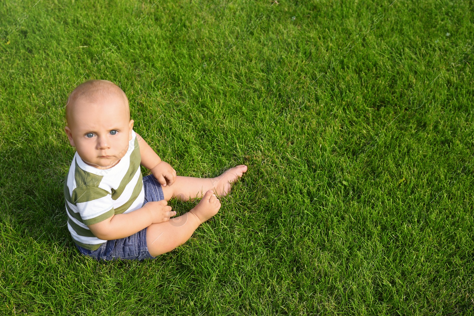 Photo of Adorable little baby sitting on green grass outdoors