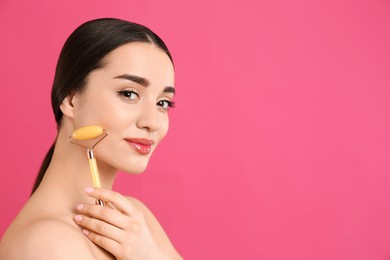 Woman using natural jade face roller on pink background, space for text