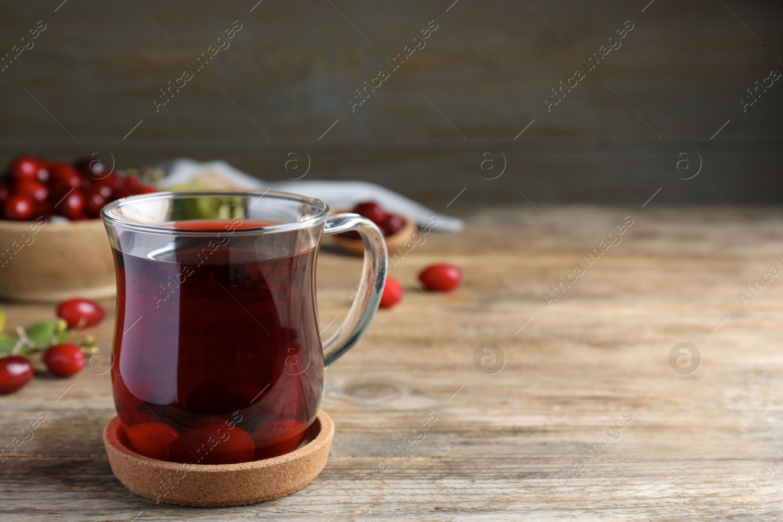 Photo of Glass cup of fresh dogwood tea with berries on wooden table. Space for text