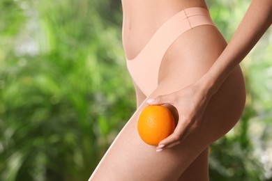 Photo of Closeup view of slim woman in underwear with orange on blurred green background, space for text. Cellulite problem concept