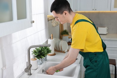 Photo of Young plumber wearing uniform repairing sink in kitchen