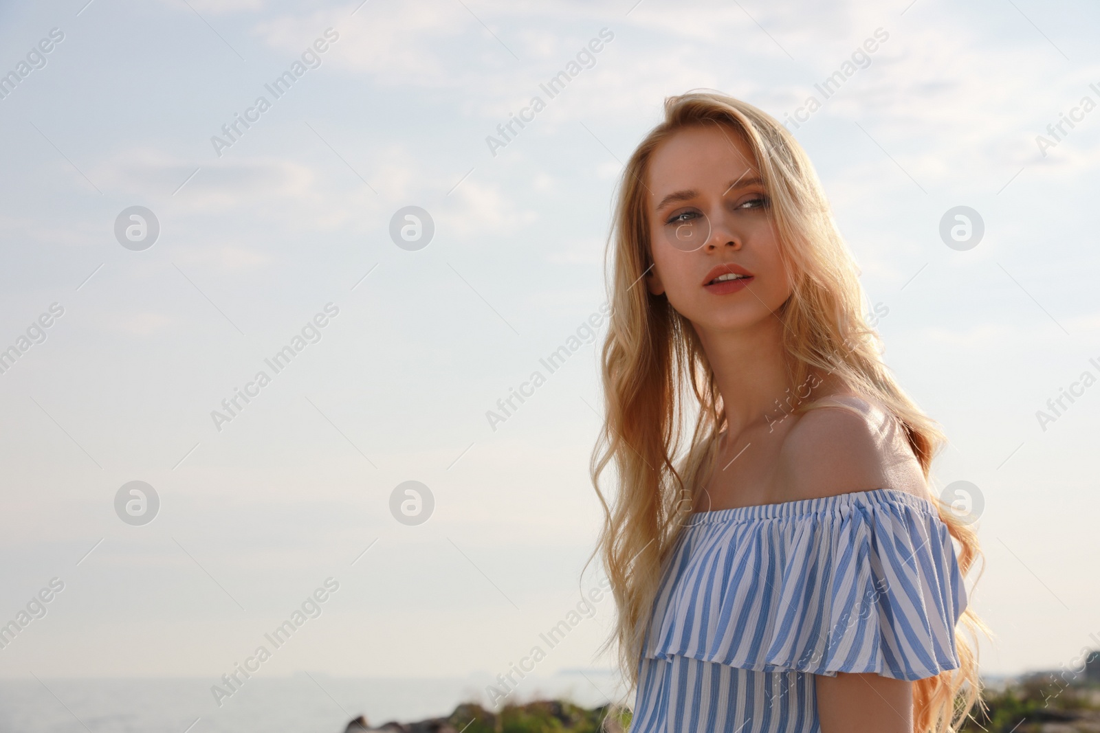 Photo of Beautiful young woman near sea on sunny day, space for text