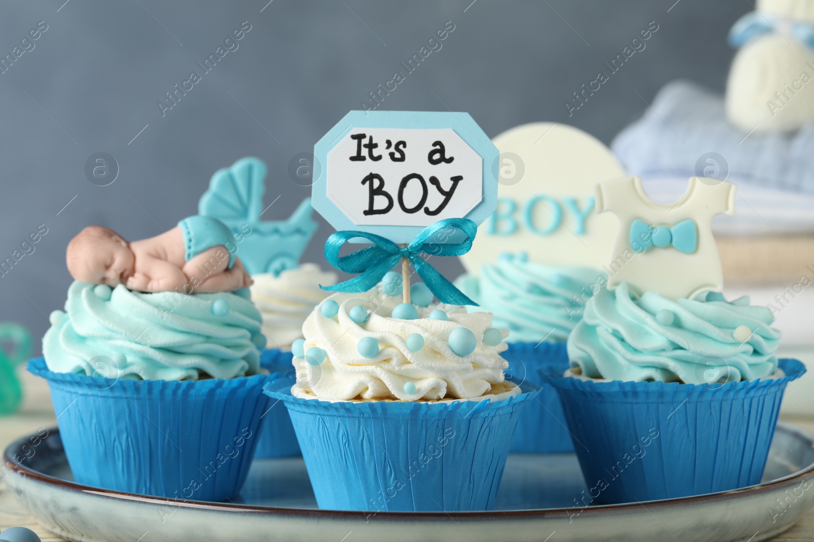 Photo of Beautifully decorated baby shower cupcakes for boy with cream on tray, closeup view